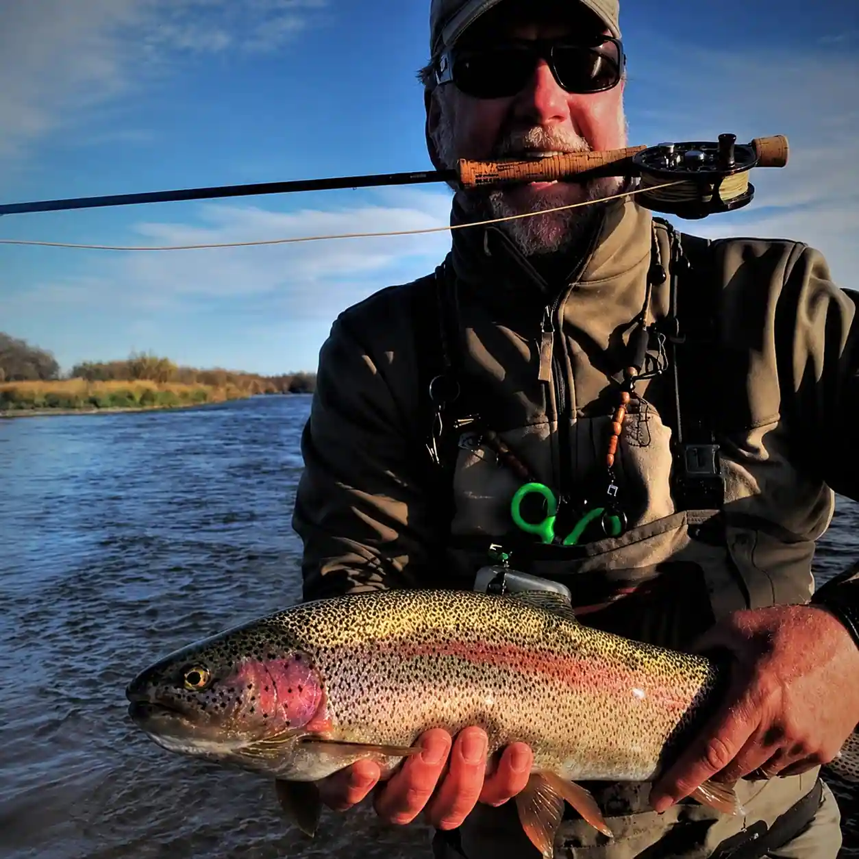 Guest holding a rainbow trout caught on a mouse pattern along a grassy Alaska riverbank